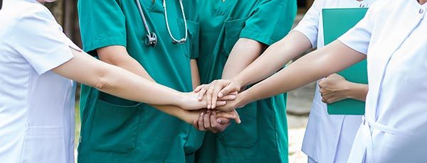 Teamwork: Krankenschwestern und Ärzte legen Hände aufeinander - Supervision in der Pflege
