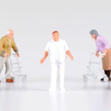 Miniaturfigur Pfleger wird hilfesuchend umringt von Pflegebedürftigen