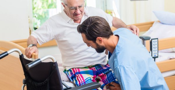Pflegeassistent hilft Senior in Rollstuhl