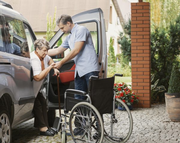 Mann hilft gehbehinderter Seniorin beim Aussteigen aus dem Auto