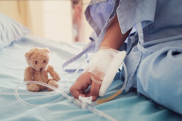 Kind sitzt mit Plüschbär auf Krankenhausbett