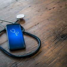 Telemedizin: Smartphone und Stethoskop auf Holztisch