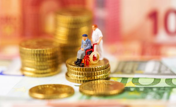 Foto: Miniaturfiguren zeigen einen Pfleger, der einen Mann im Rollstuhl fährt, diese Figuren stehen auf gestapelten Centmünzen