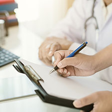 Ärztin und Helfer betrachten ein Klemmbrett und unterschreiben ein darauf befindliches Dokument