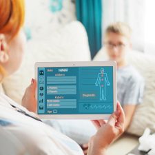 Arzt mit digitaler Patientenakte, im Hintergrund junger Patient