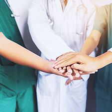 Mehrere Pflegekräfte legen die Hände in der Mitte übereinander