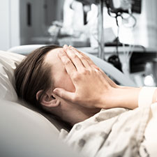 Foto: Frau im Krankenbett hat das Gesicht hinter den Händen verborgen