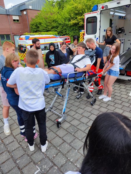 Schüler und Schülerinnen schieben einen Mitschüler auf einer Fahrtrage in einen Rettungswagen
