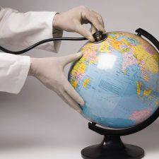 Ein Stetoskop wird von einem Arzt an eine Weltkugel gehalten