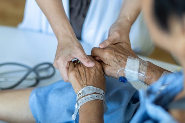 Pflegekraft hält die Hände eines Patienten, der im Krankenbett liegt
