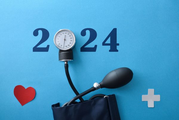 Blutdruckmessgerät, Jahreszahl und Papierherz liegen auf blauem Tisch