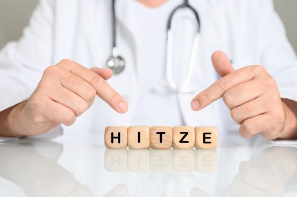 Arzt sitzt an weißem Tisch hinter Holzwürfeln auf denen Hitze stehta