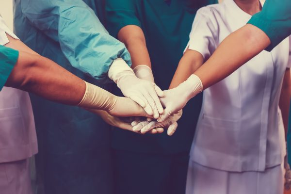 Pfleger, Ärzte und Betreuer legen im Kreis stehend ihre Hände aufeinander.
