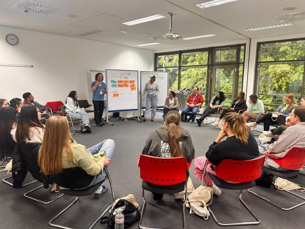 Teilnehmerinnen und Teilnehmer sitzen auf Stühlen im Kreis während eines Vortrags