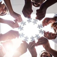 Menschen stehen im Kreis und strecken jeweils ein Puzzleteil in die Mitte