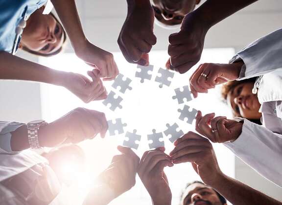 Menschen stehen im Kreis und strecken jeweils ein Puzzleteil in die Mitte