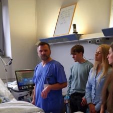 Gruppe Schüler mit Pfleger bei einer Mitmachstation an einem Krankenbett