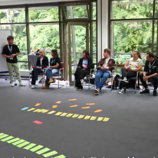 Workshopteilnehmerinnen sitzen auf Stühlen und hören Referent zu der an einem Whiteboard steht